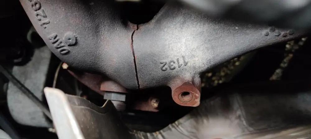 The image shows a close-up view of a cracked exhaust manifold, highlighting a visible split along the surface of the metal component.