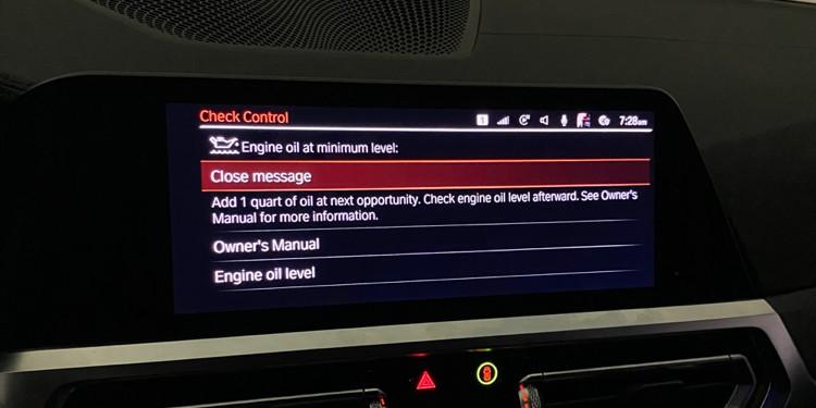  A vehicle’s dashboard display showing a warning message about the engine oil being at a minimum level, with instructions to add oil.