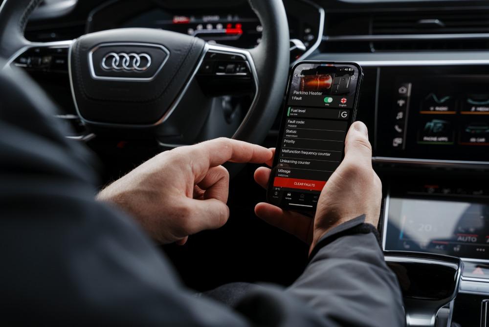  ChatGPT A person in an Audi holding a smartphone with the OBDeleven car diagnostic app displaying vehicle diagnostics and fault codes.