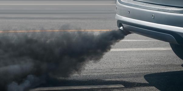 Exhaust from a car's tailpipe emitting a thick cloud of black smoke, indicative of an engine malfunction or excessive pollution, on a road surface.