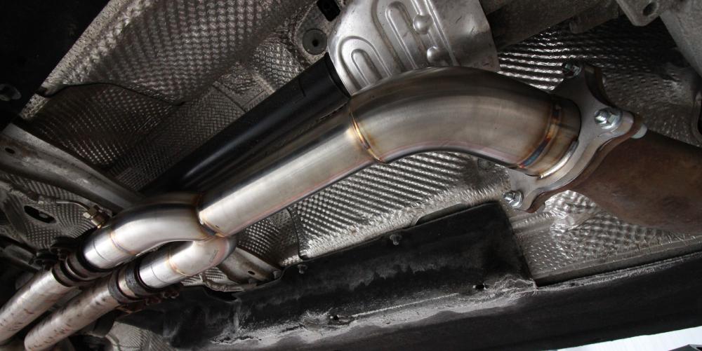 Close-up view of the underside of a car showing a stainless steel aftermarket exhaust component, with surrounding heat shielding materials.