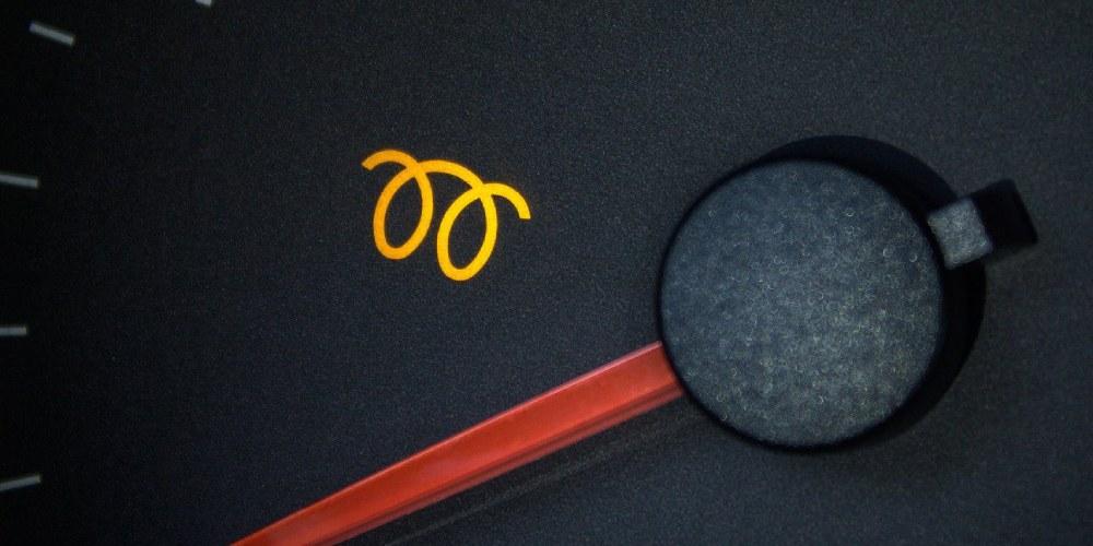 A close-up view of a car dashboard displaying an illuminated glow plug warning light, symbolized by a yellow icon resembling a coiled wire