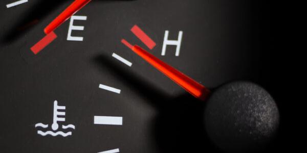 Close-up of a car's coolant temperature gauge indicating engine overheating, with the needle approaching the red 'H' zone.