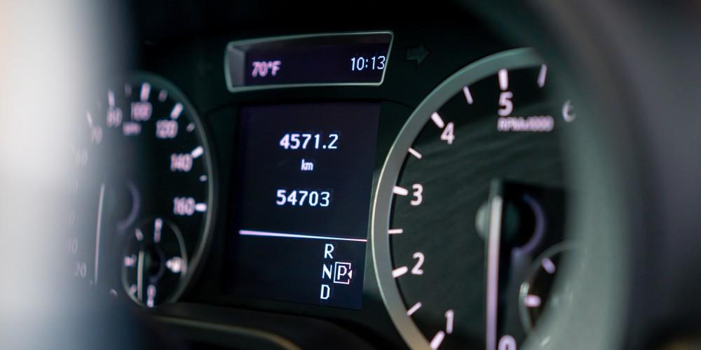  Close-up of a car's digital instrument panel showing the odometer, a tachometer, and gear indicator, with a blurred speedometer in the background.