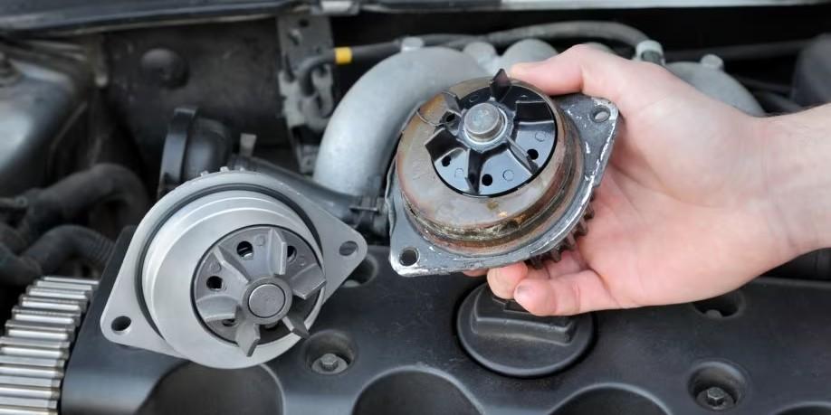A person's hand holding a corroded car water pump next to a new one, highlighting the comparison between the two components.