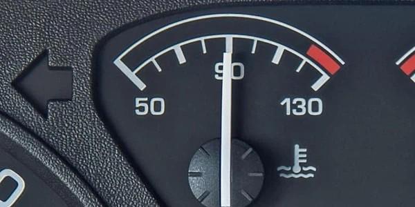 Close-up of a vehicle’s temperature gauge on the dashboard, showing the needle pointing towards the mid-range with a coolant temperature warning icon nearby.