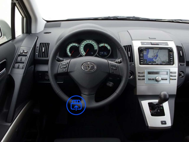 The image shows the interior of a Toyota Corolla Verso, highlighting the OBD-II port location beneath the dashboard near the driver’s footwell.