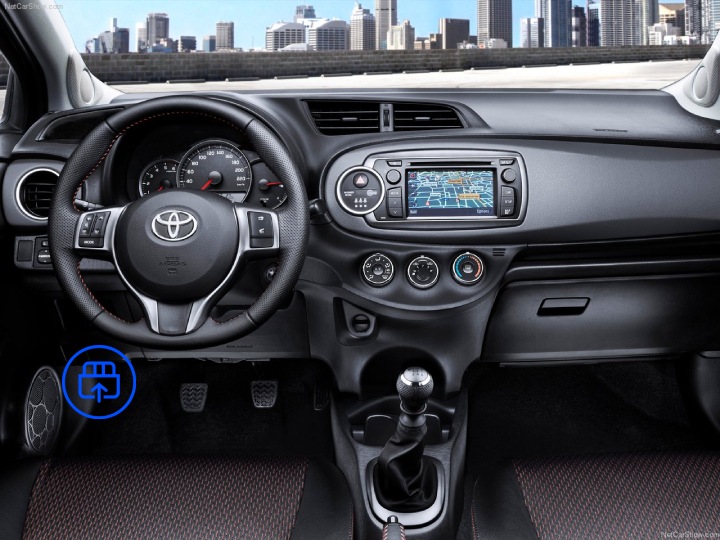  The image shows the interior of a Toyota Yaris, highlighting the OBD-II port location beneath the dashboard near the driver’s footwell.