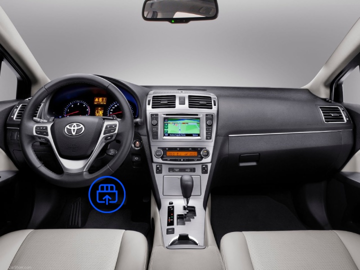 The image shows the interior of a Toyota Avensis, highlighting the OBD-II port location beneath the dashboard near the driver’s footwell.