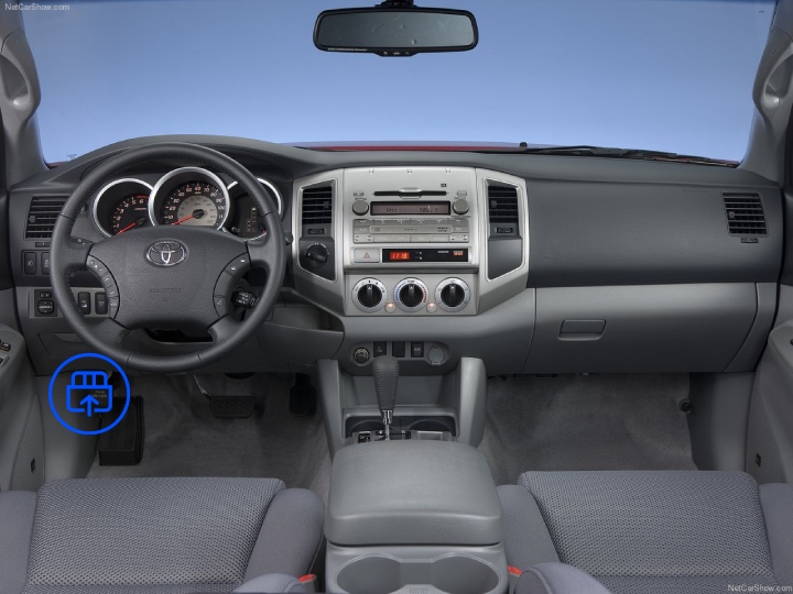  The image shows the interior of a Toyota Tacoma, highlighting the OBD-II port location beneath the dashboard near the driver’s footwell.