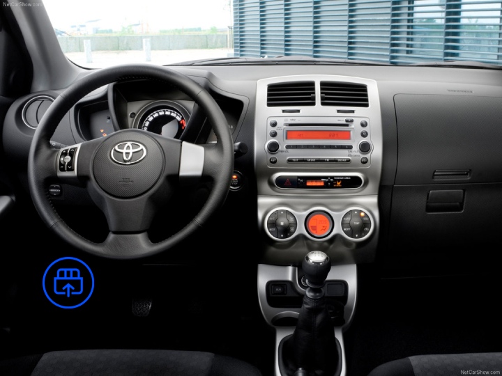 The image shows the interior of a Toyota Urban Cruiser, highlighting the OBD-II port location beneath the dashboard near the driver’s footwell.